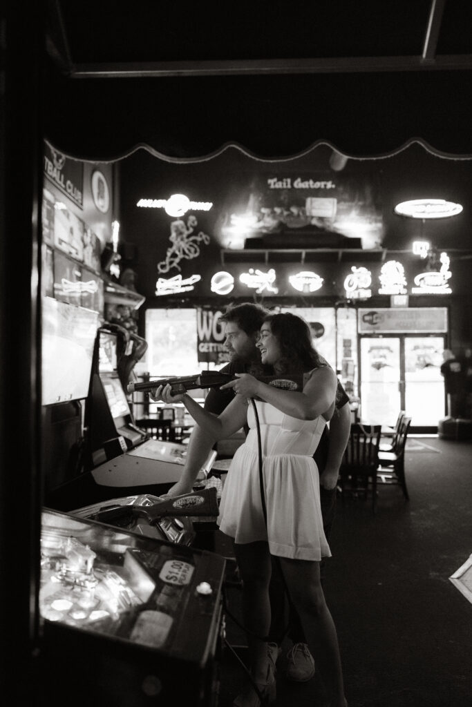 Black and white candid of couple standing close together near jukebox, arms around each other