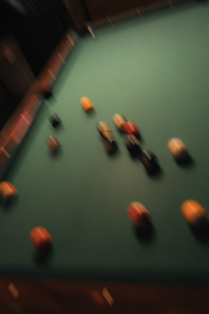 Motion-blurred pool balls scattering across green felt during break shot