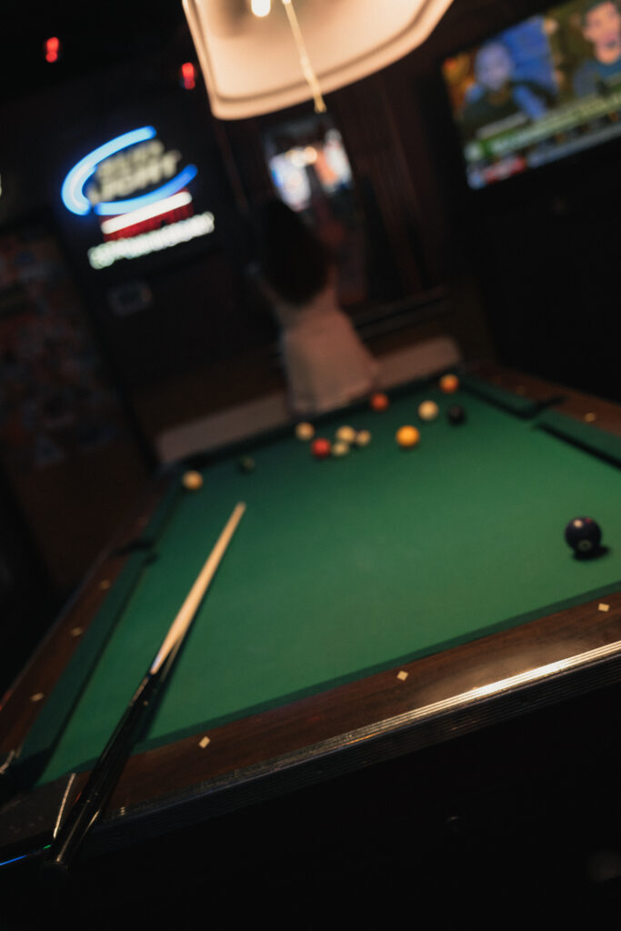 Pool table and neon beer sign glowing in dimly lit dive bar, moody engagement photography