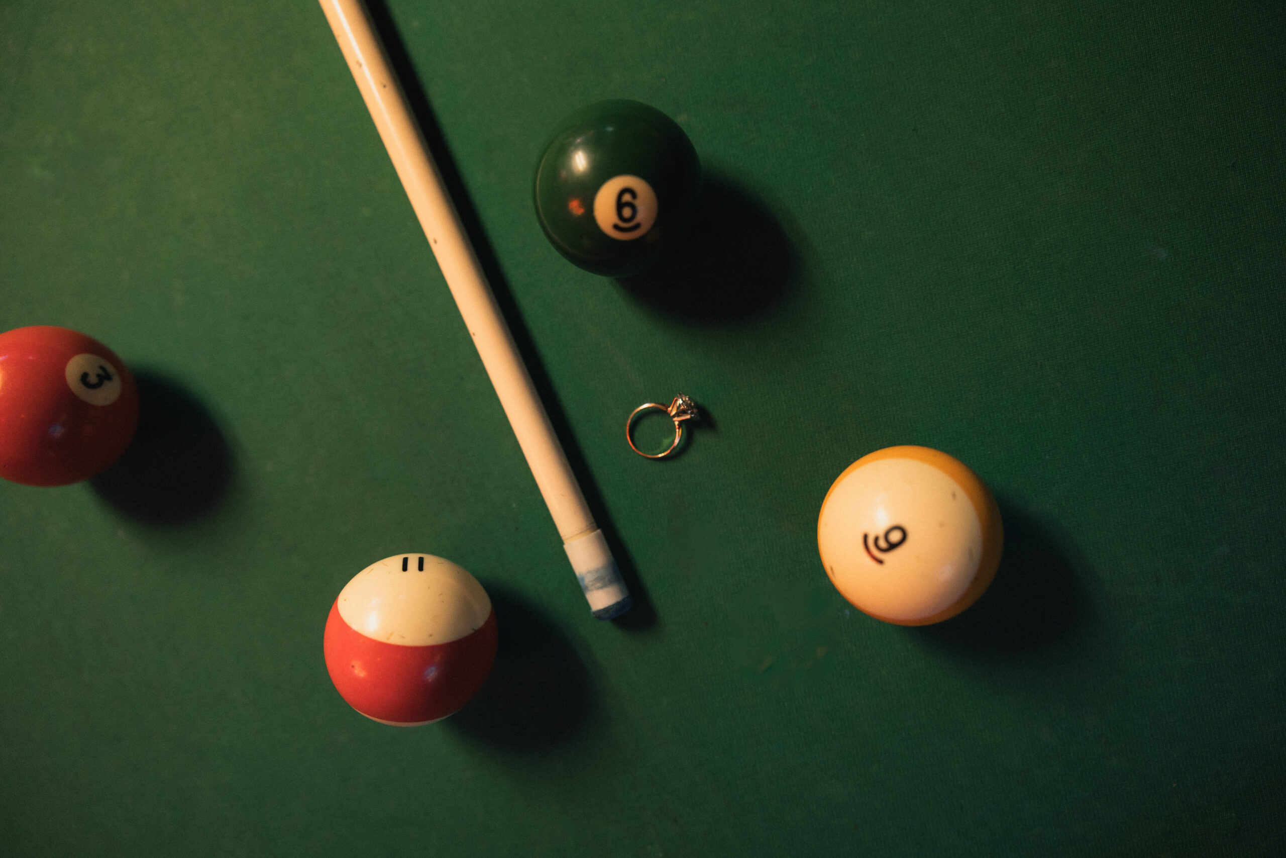 Racked pool balls with striped and solid ball resting nearby, cue stick crossing frame, dive bar engagement session