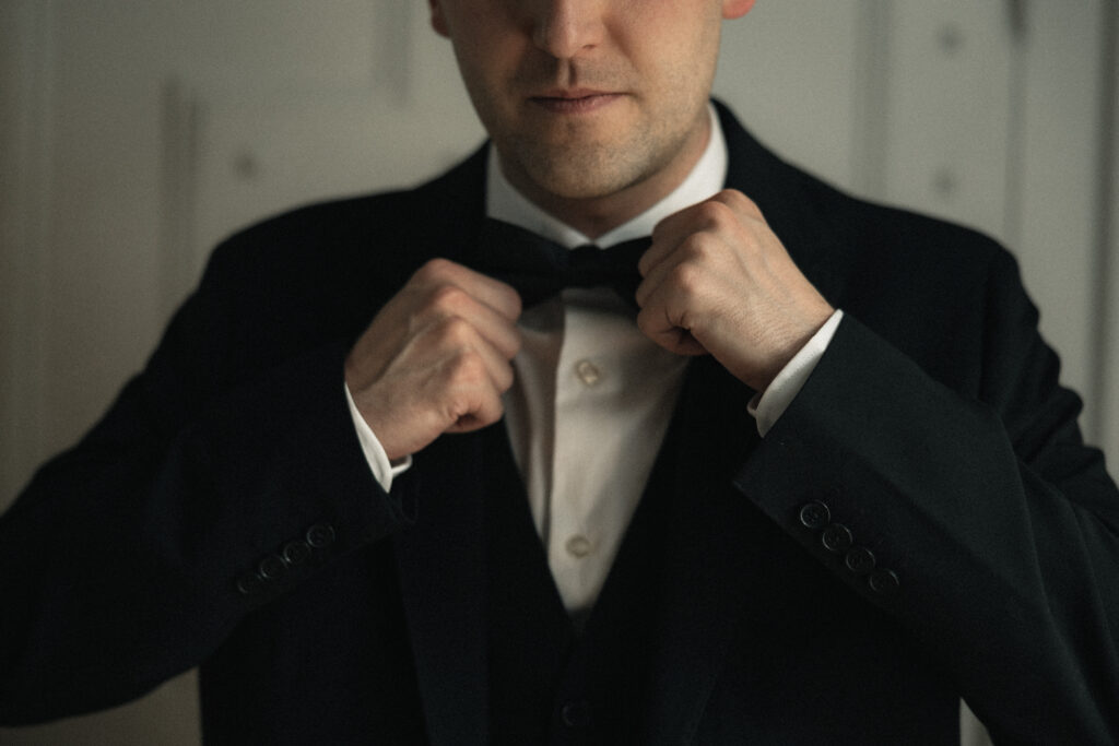 Groom adjusting bow tie close-up, black tuxedo wedding portrait