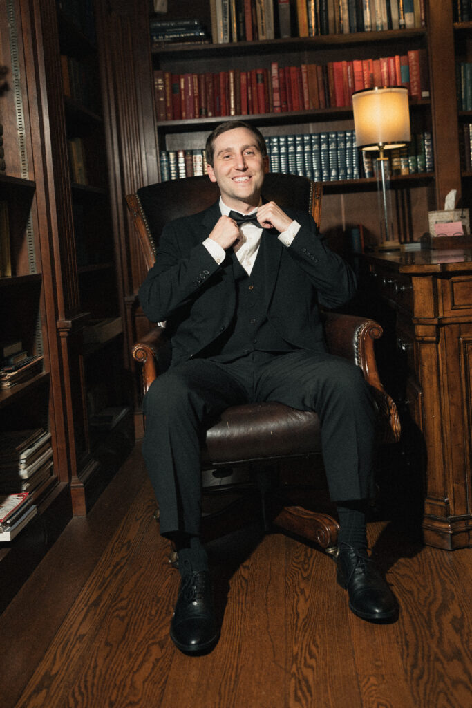 Groom smiling in library study before wedding ceremony