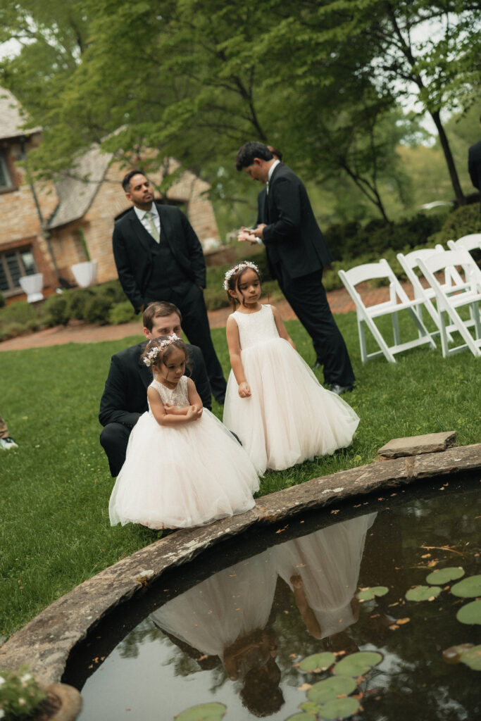 Flower girls and groomsmen by garden pond before wedding ceremony