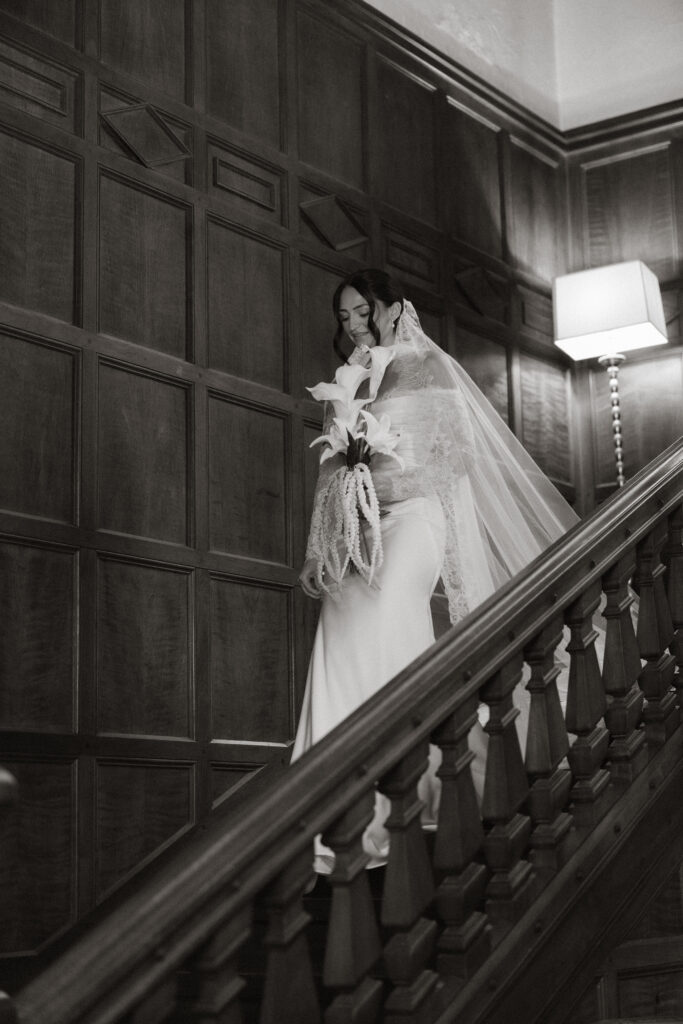 Bride descending wooden staircase holding calla lily bouquet, black and white