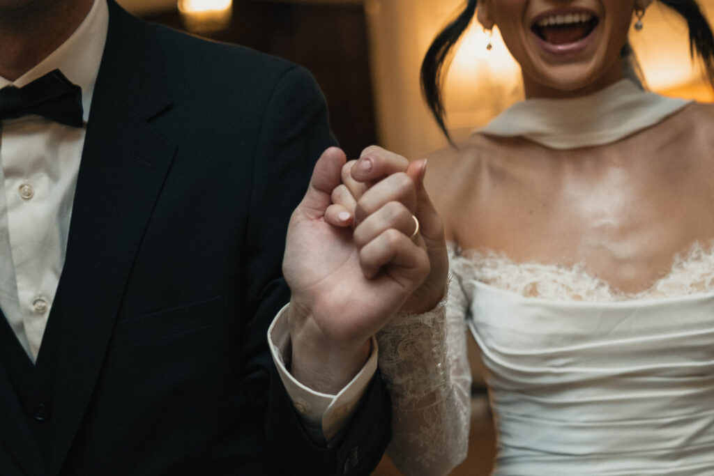 Close up of bride and groom holding hands, wedding ring detail