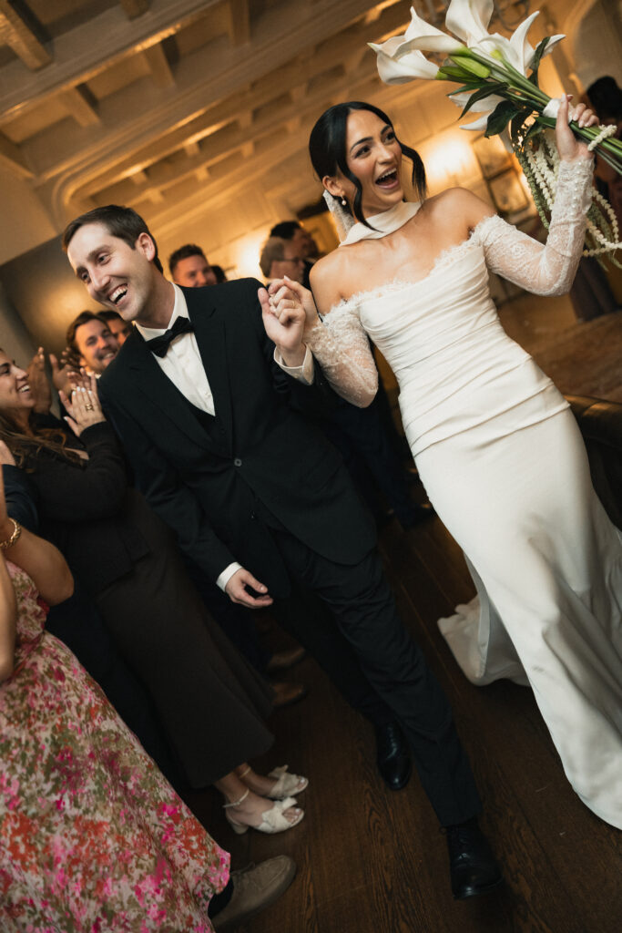 Bride and groom walking through reception cheered on by guests