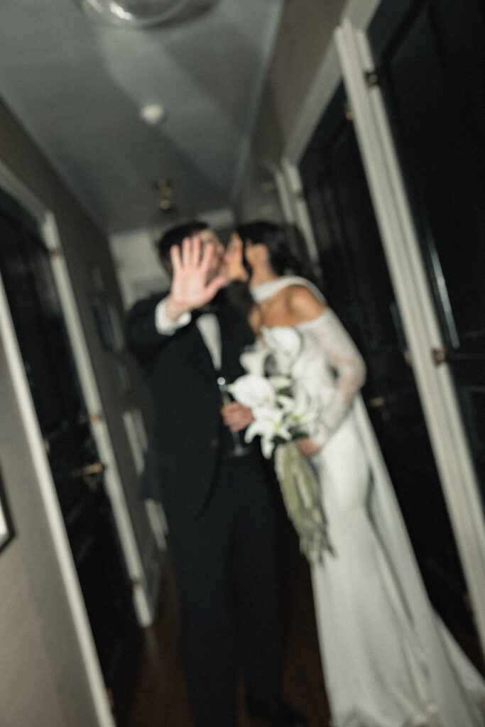 Bride and groom sharing a kiss in hallway, groom holding bouquet