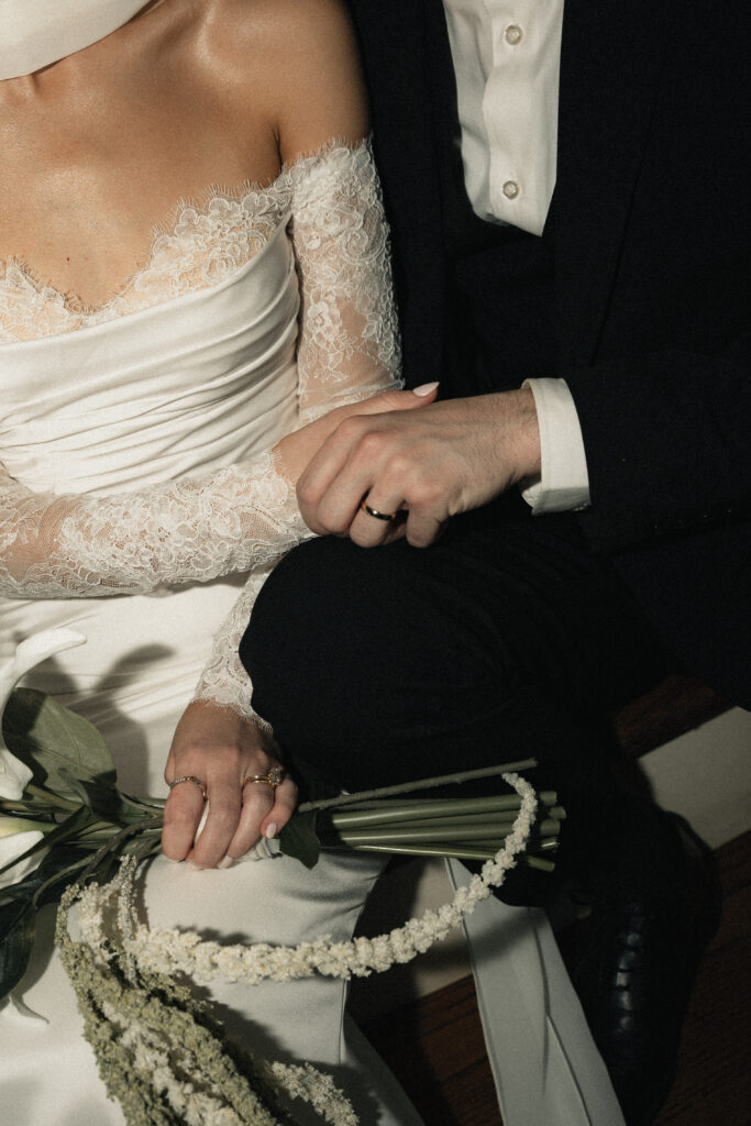 Bride and groom holding bouquet and hands seated together, close up