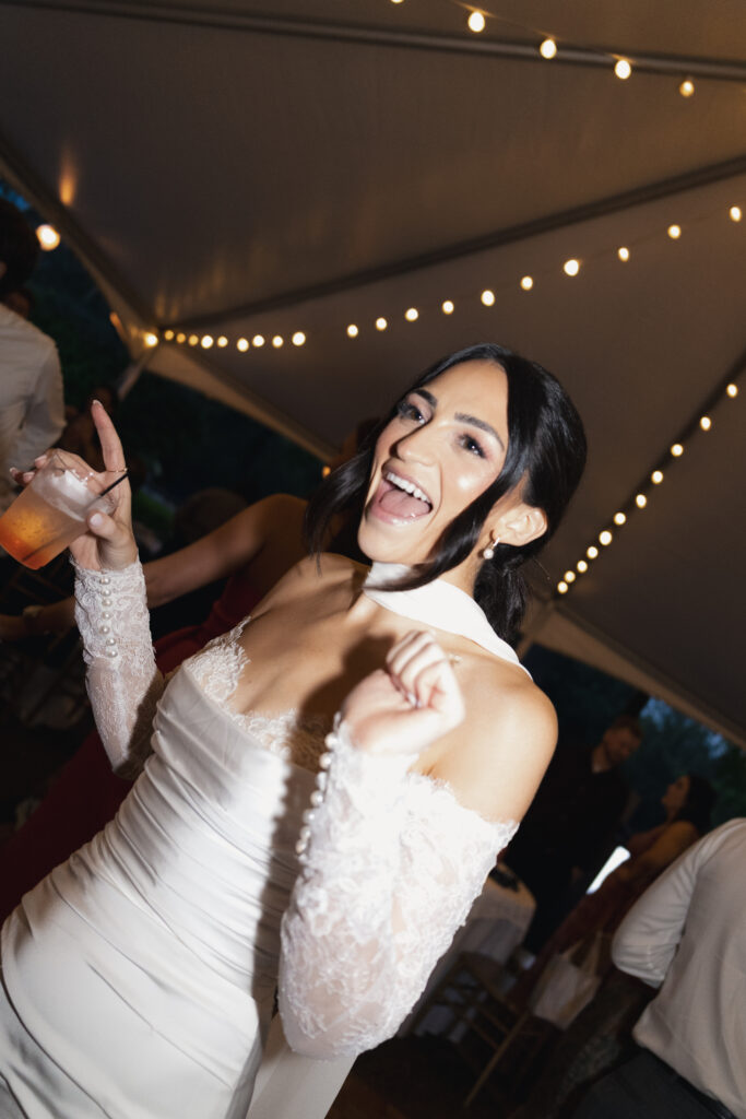 Bride laughing and dancing under string lights at wedding reception