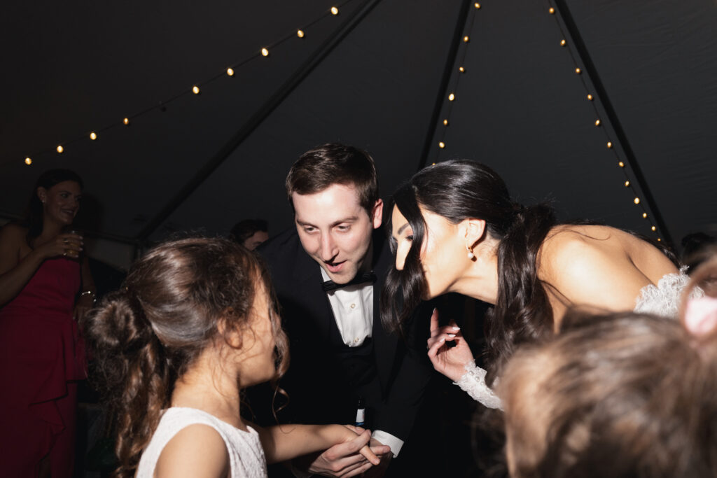 Bride and groom dancing with wedding guest under string lights