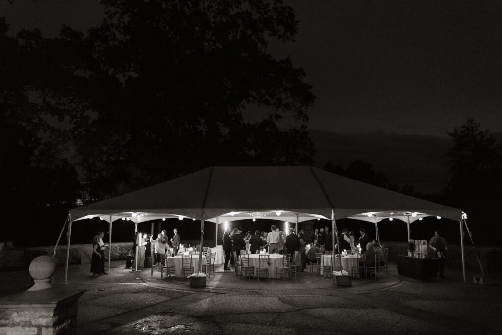 Outdoor wedding reception tent at night with string lights, black and white