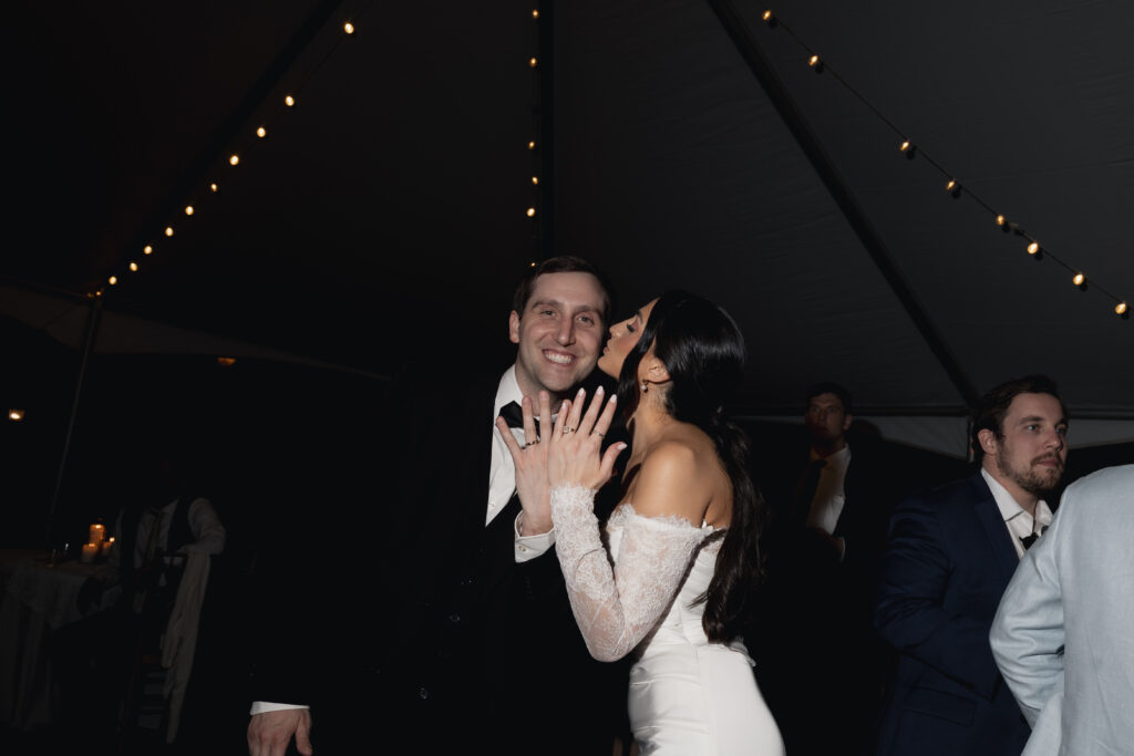 Bride showing off wedding ring, kissing groom's cheek