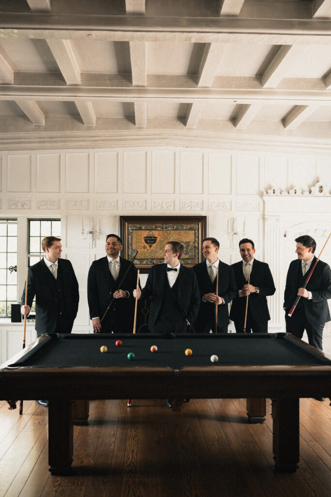 Groomsmen playing pool in wood-paneled room, wedding day details